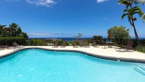 A clear blue pool with lounge chairs and a view of the ocean.
