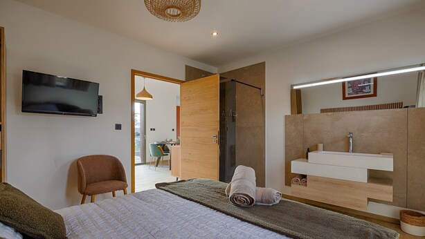 A modern hotel room with a bed, a TV, a bathroom with a sink, and a chair.