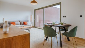 A modern living room with a sofa, a dining table with chairs, a wooden coffee table, and a large window.