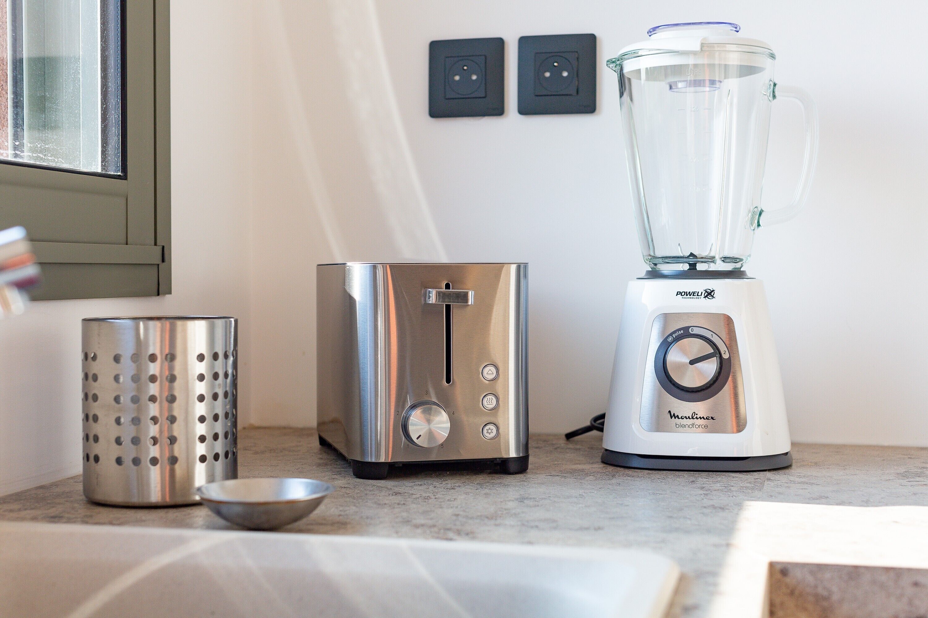 A kitchen with a toaster, a blender, and a colander on the counter.