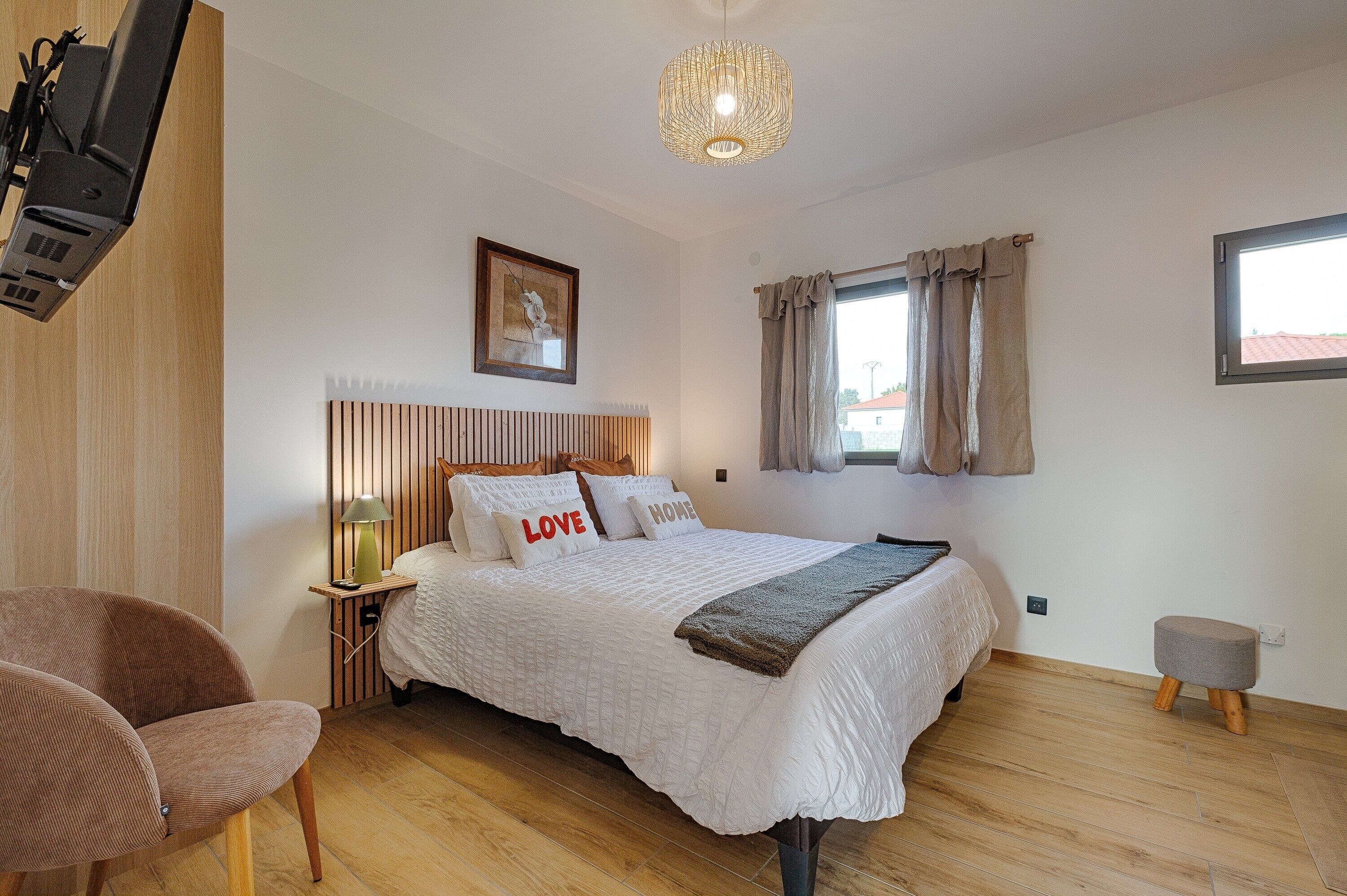 A bedroom with a bed, a chair, a bedside table with a lamp, a picture on the wall, and a window with curtains.