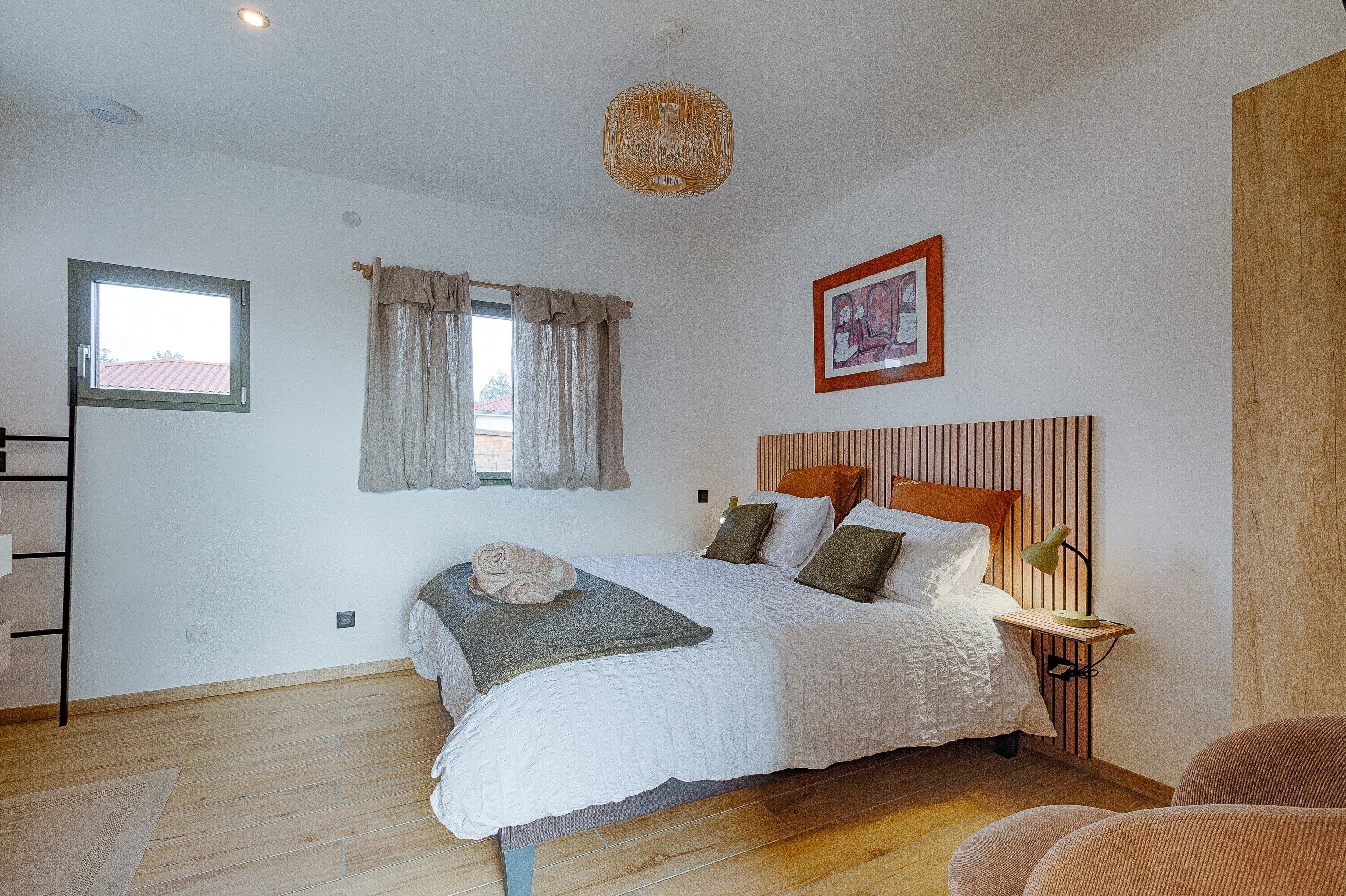 Een slaapkamer met een bed, een nachtkastje met een lamp, een raam met gordijnen, een lijst met een afbeelding aan de muur en een houten vloer.