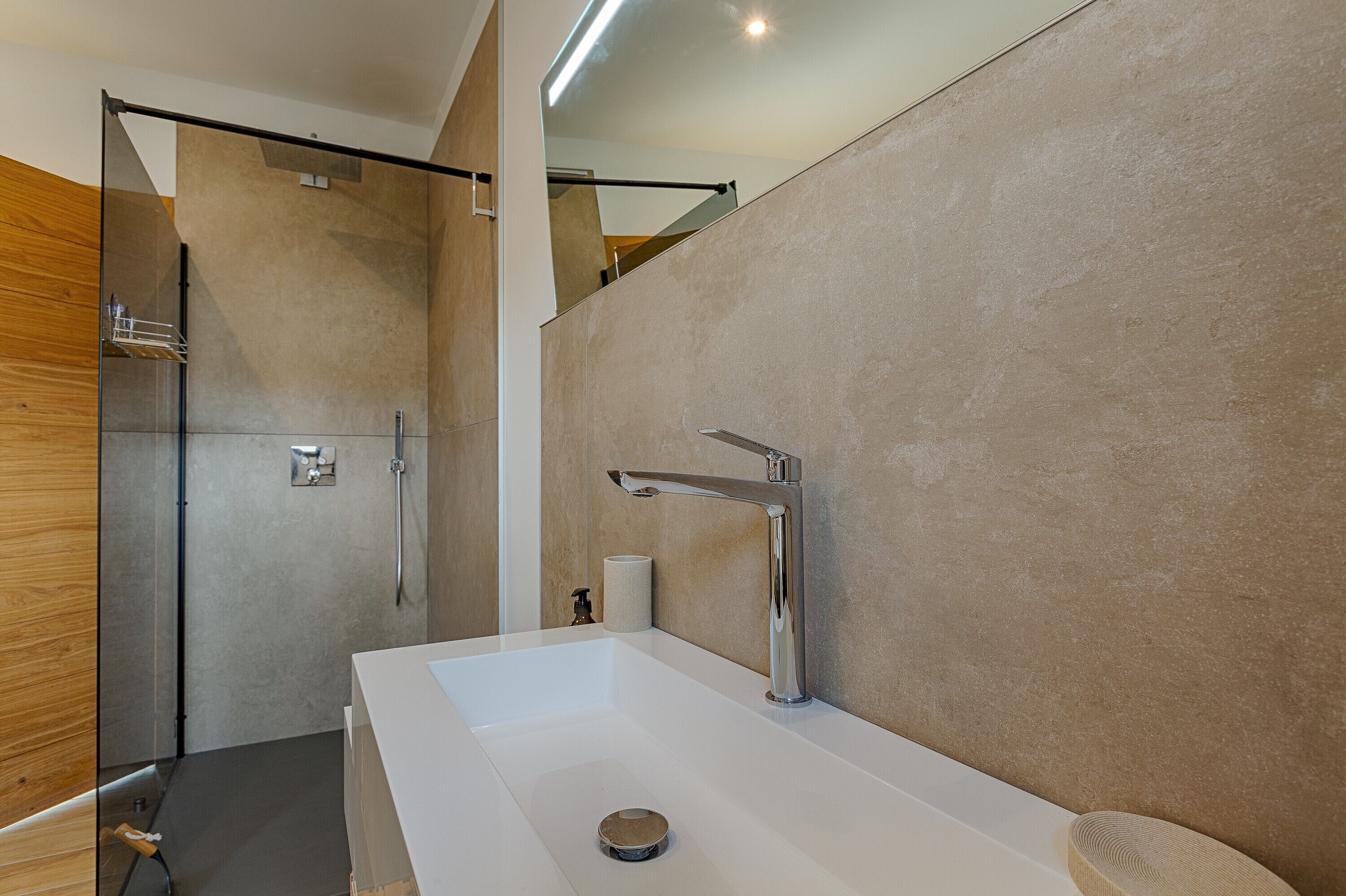 Ein modernes Badezimmer mit einem großen, weißen Waschbecken, einem Chrom-Wasserhahn und einer Duschkabine aus Glas.