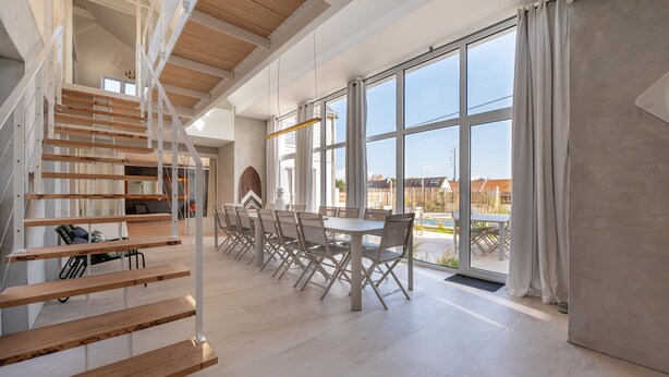 Une pièce spacieuse dotée d’une grande fenêtre, d’un escalier et d’un coin repas avec des chaises et une table.