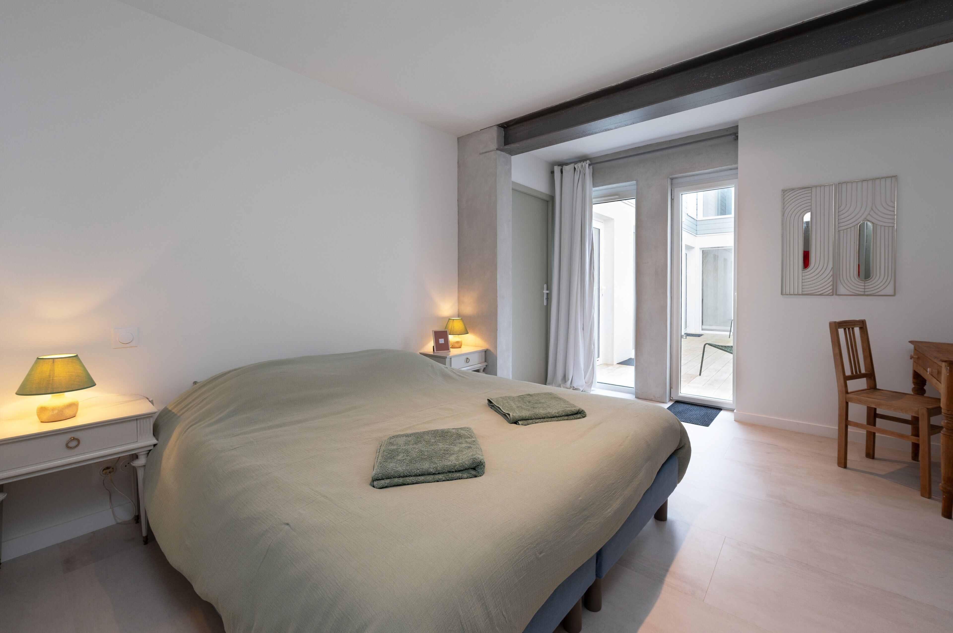 Ein Schlafzimmer mit Bett, Nachttischlampen, einem Sessel und Blick ins Freie.