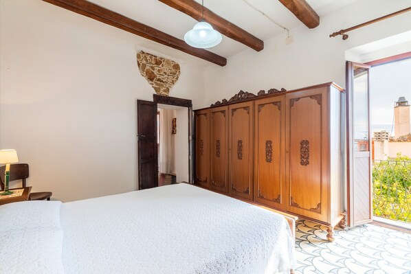 A bedroom with a bed, wooden wardrobe, and a view through an open door.