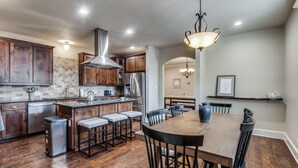 A modern kitchen with wooden cabinets, stainless steel appliances, and a central island with bar stools. - NEW! Charming Retreat Near Dickie's Arena – Cozy & Stylish Fort Worth Getaway (Fort Worth)
