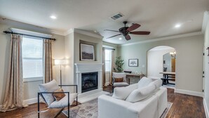 A living room with a fireplace, a ceiling fan, and a dining area with a table and chairs. - NEW! Charming Retreat Near Dickie's Arena – Cozy & Stylish Fort Worth Getaway (Fort Worth)