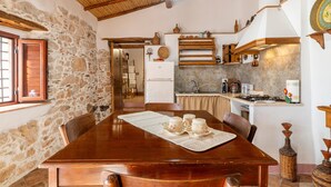 Une cuisine rustique aux murs de pierre, avec des poutres en bois, et un coin repas comprenant une table et des chaises en bois.