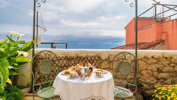 Une table dressée pour le petit-déjeuner, avec vue sur la mer, un mur en pierre et une pergola en métal.