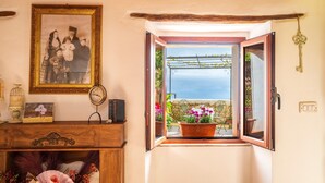 Une pièce comprenant un meuble en bois, une photographie encadrée, une horloge et une fenêtre donnant sur un balcon et des plantes.