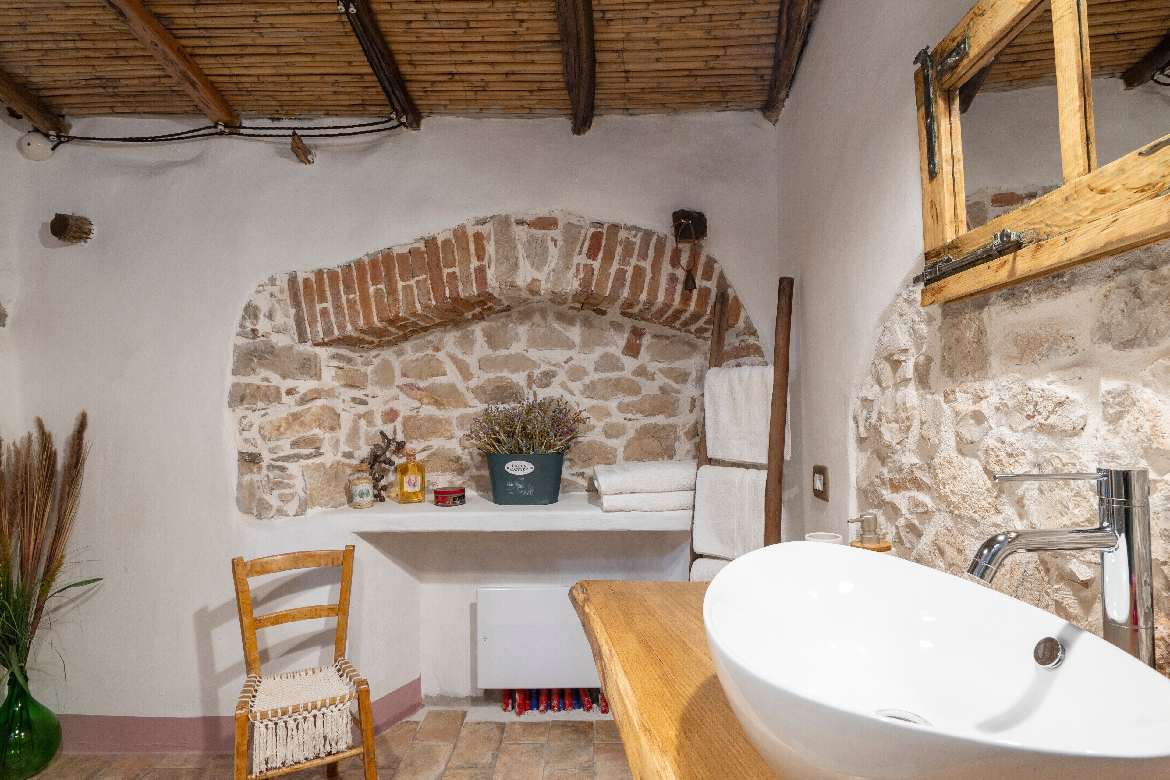 A bathroom with a stone arch, a wooden chair, a sink, and a mirror.
