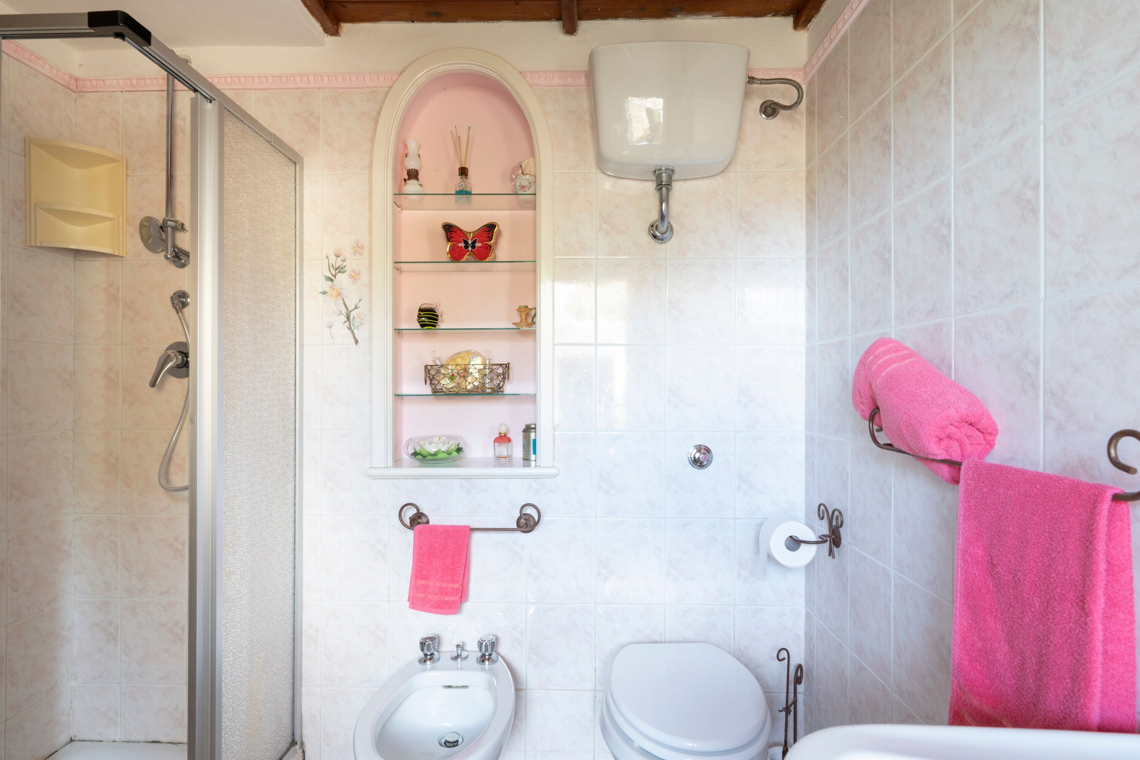 A bathroom with a shower, bidet, toilet, and a shelf with decorative items.