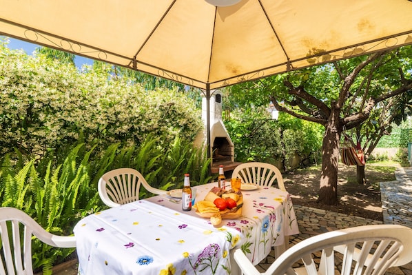 An outdoor dining area with a table set under a canopy, surrounded by lush greenery.