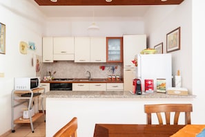 A kitchen with white cabinets, a granite countertop, a microwave, a coffee machine, and a dining area with a wooden table and chairs.