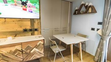 Ein modernes Zimmer mit Fernseher, einem Holzkabinett, einem Tisch mit Stühlen und einer dekorativen Wandgestaltung.