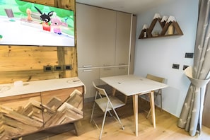 Una habitación moderna con televisión, un mueble de madera, una mesa con sillas y un elemento decorativo en la pared.