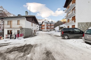 Una calle nevada con edificios, un coche aparcado y una montaña al fondo.