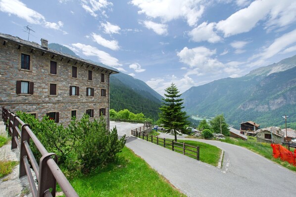 A stone building with multiple windows and a paved road leading to a mountain view.