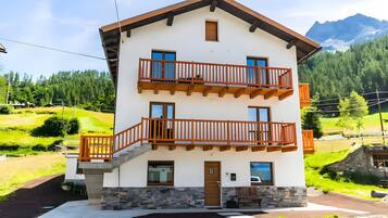 Un bâtiment à deux étages, doté de fondations en pierre, de balcons en bois et offrant une vue sur un paysage montagneux.