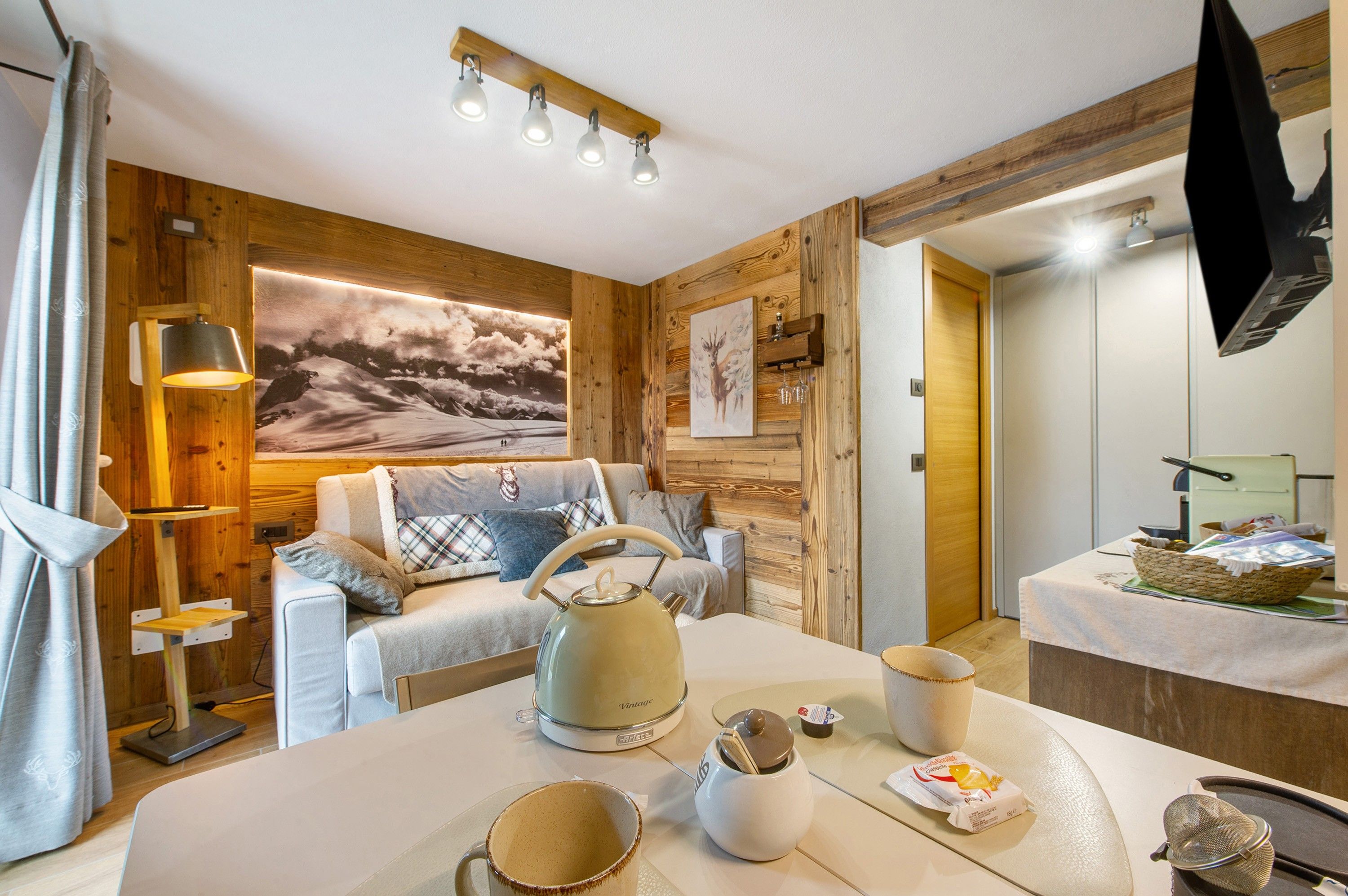 Une pièce chaleureuse avec un mur en bois, un grand tableau, un canapé, une bouilloire et une table sur laquelle se trouvent divers objets.