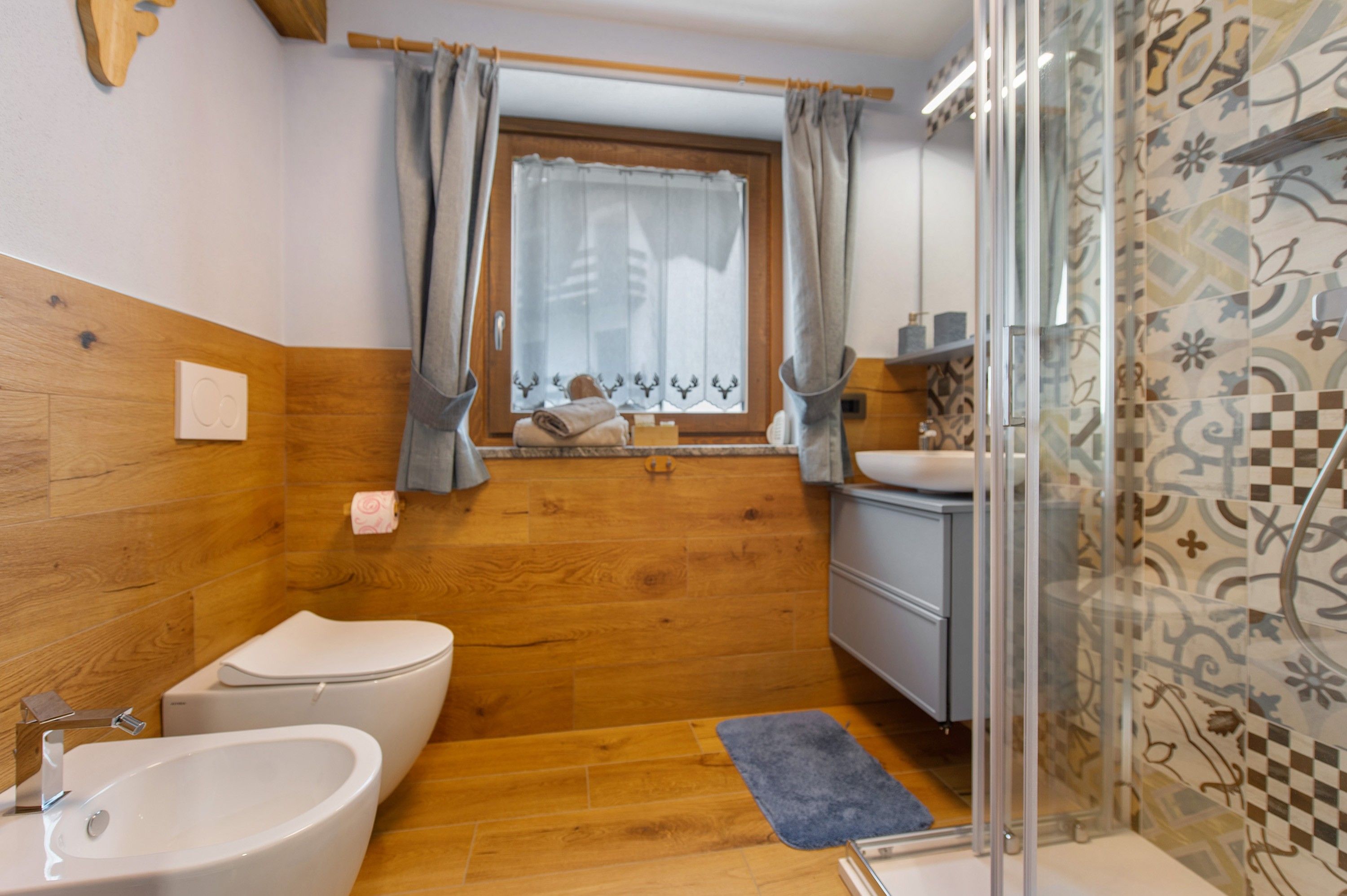 Un bagno con pavimento in legno, un WC bianco, un bidet, un lavandino e una doccia con porta in vetro.
