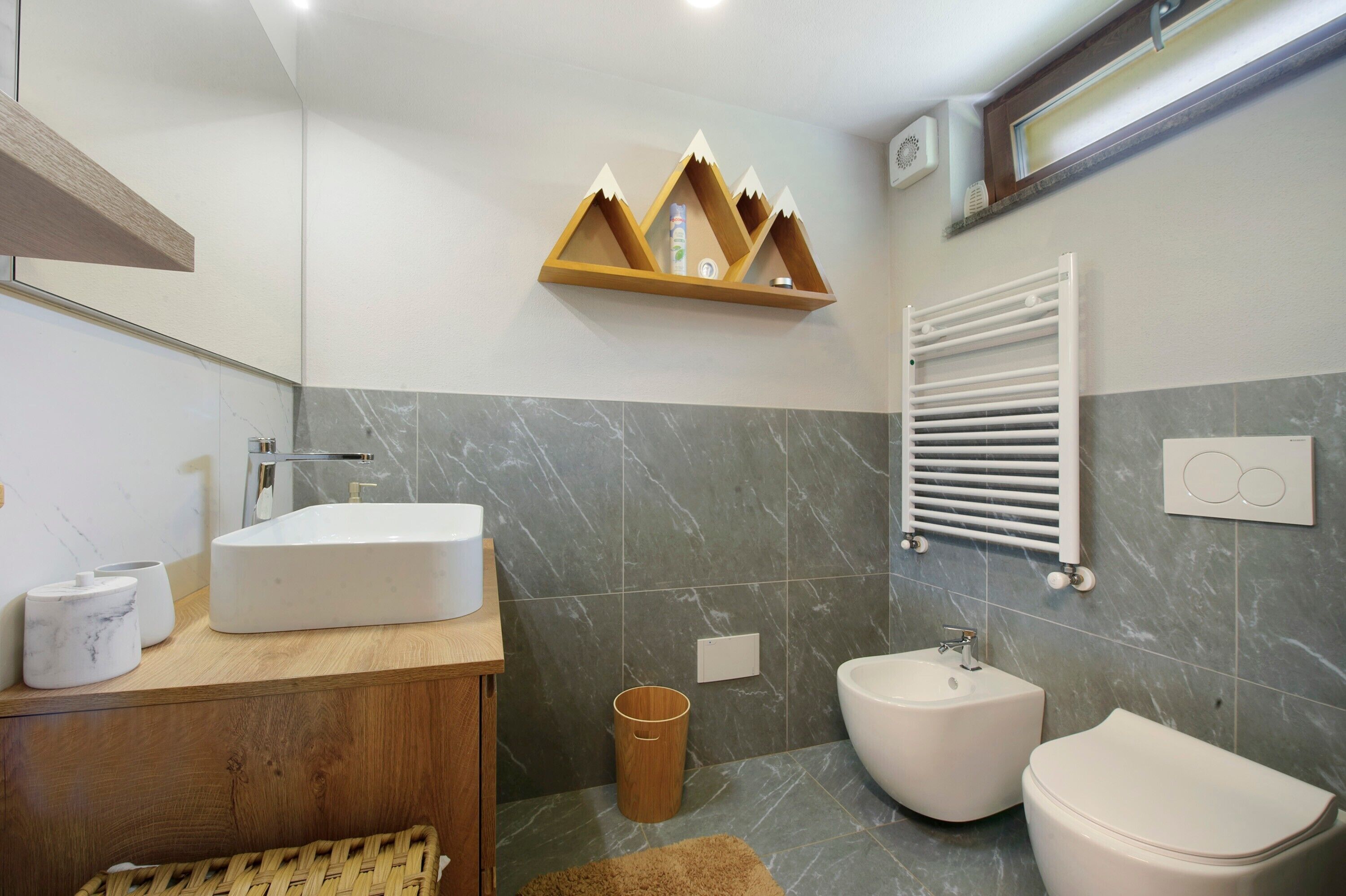 Een badkamer met een houten wastafelmeubel, een witte wastafel, een toiletbrons, een toilet en een handdoekhouder.