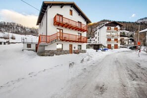 Un edificio a due piani con il terreno innevato, una scala che conduce a un balcone e un cielo sereno.