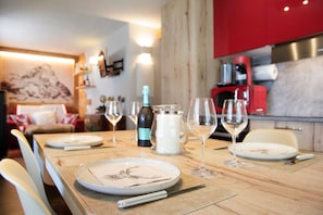 Une table à manger dressée avec des assiettes, des verres à vin et une bouteille, avec une cuisine en arrière-plan.