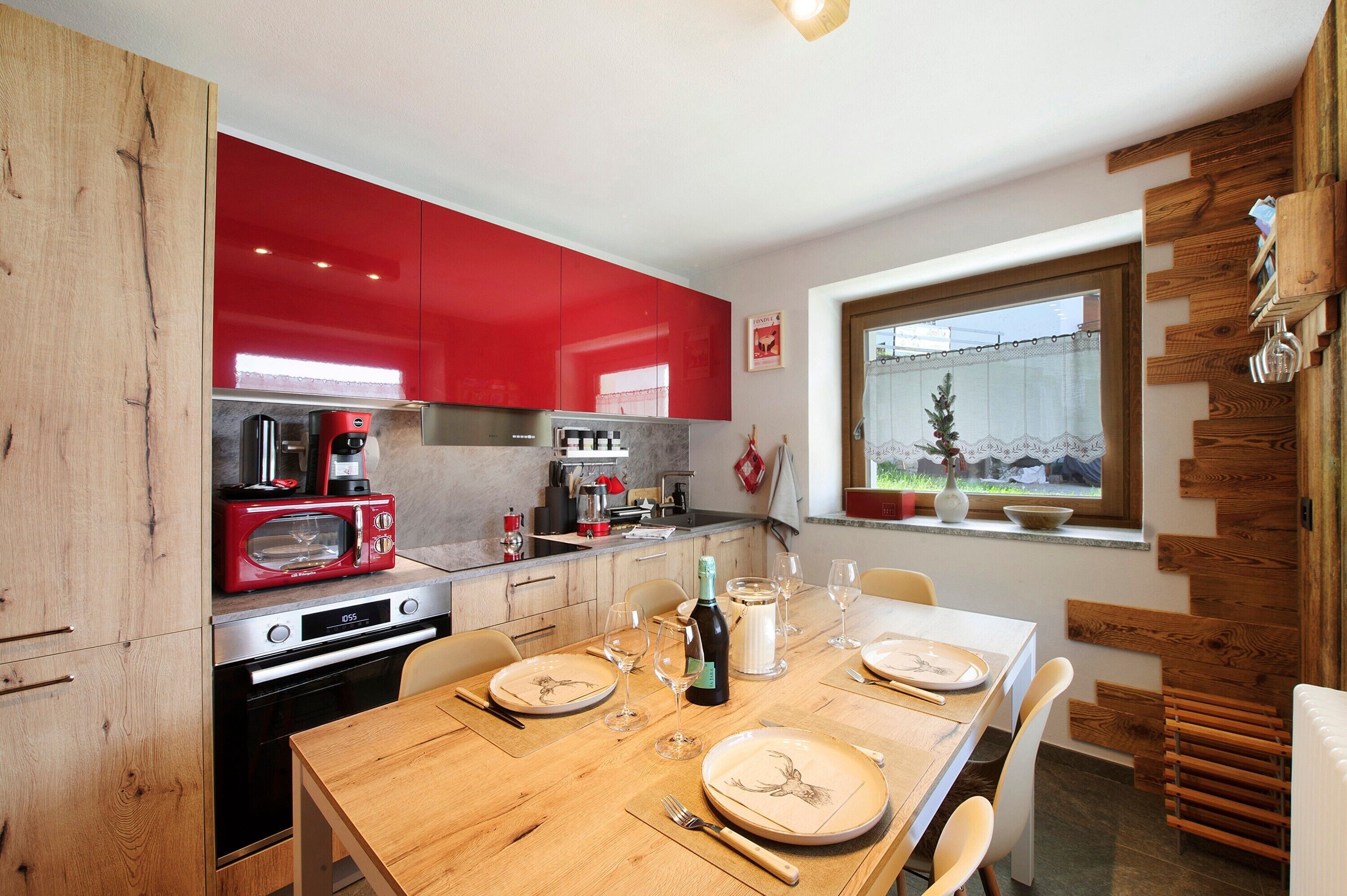 A modern kitchen with red cabinets, a dining table set for four, and a window with a view of mountains.
