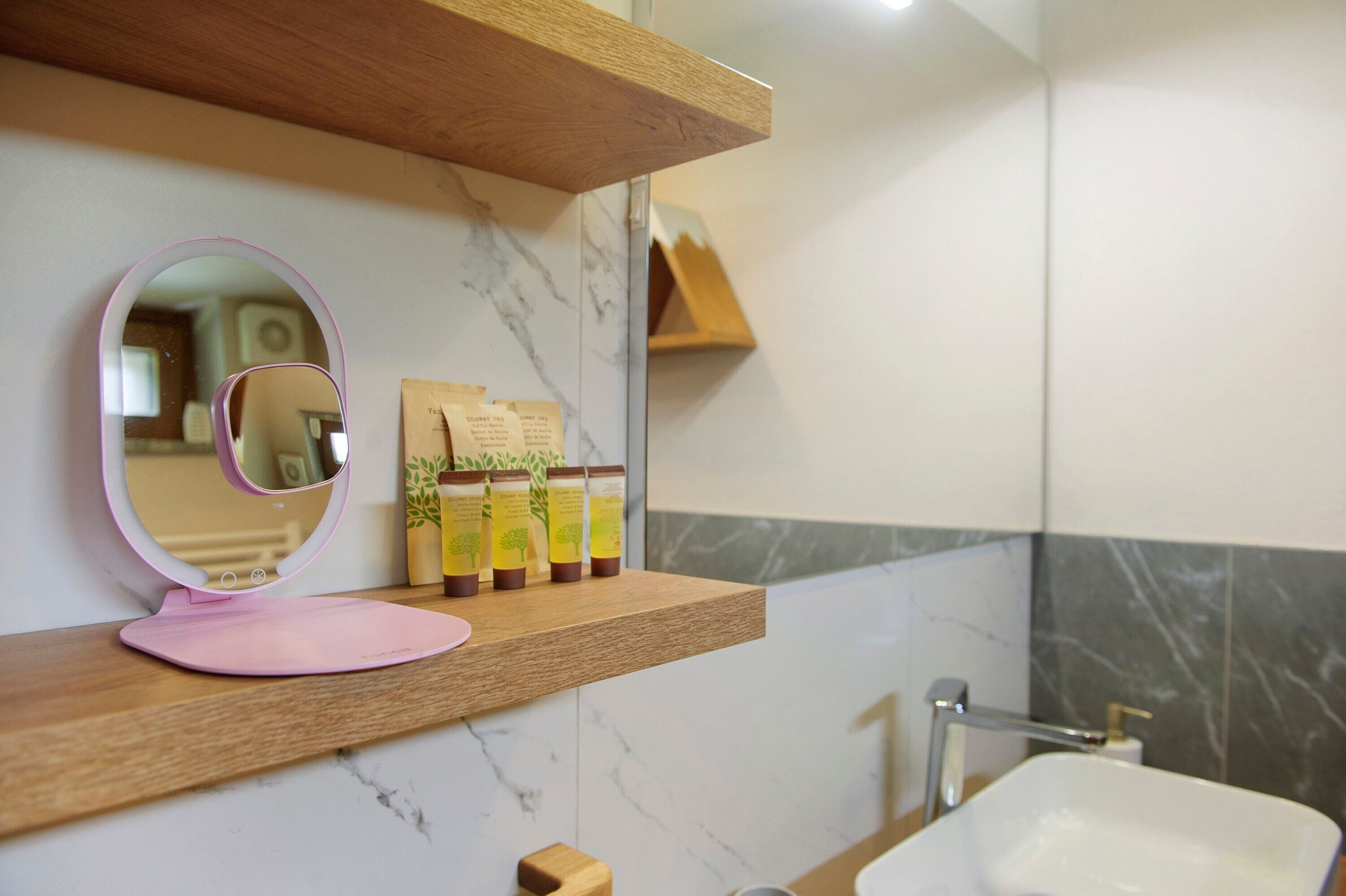 A bathroom with a wooden shelf, a mirror, toiletries, and a sink.