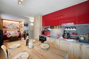 Une cuisine moderne avec des meubles rouges, une table à manger en bois pour quatre personnes et un coin salon chaleureux avec une cheminée.
