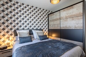 A modern bedroom with a geometric patterned wall, a large bed with multiple pillows, and a wooden headboard.