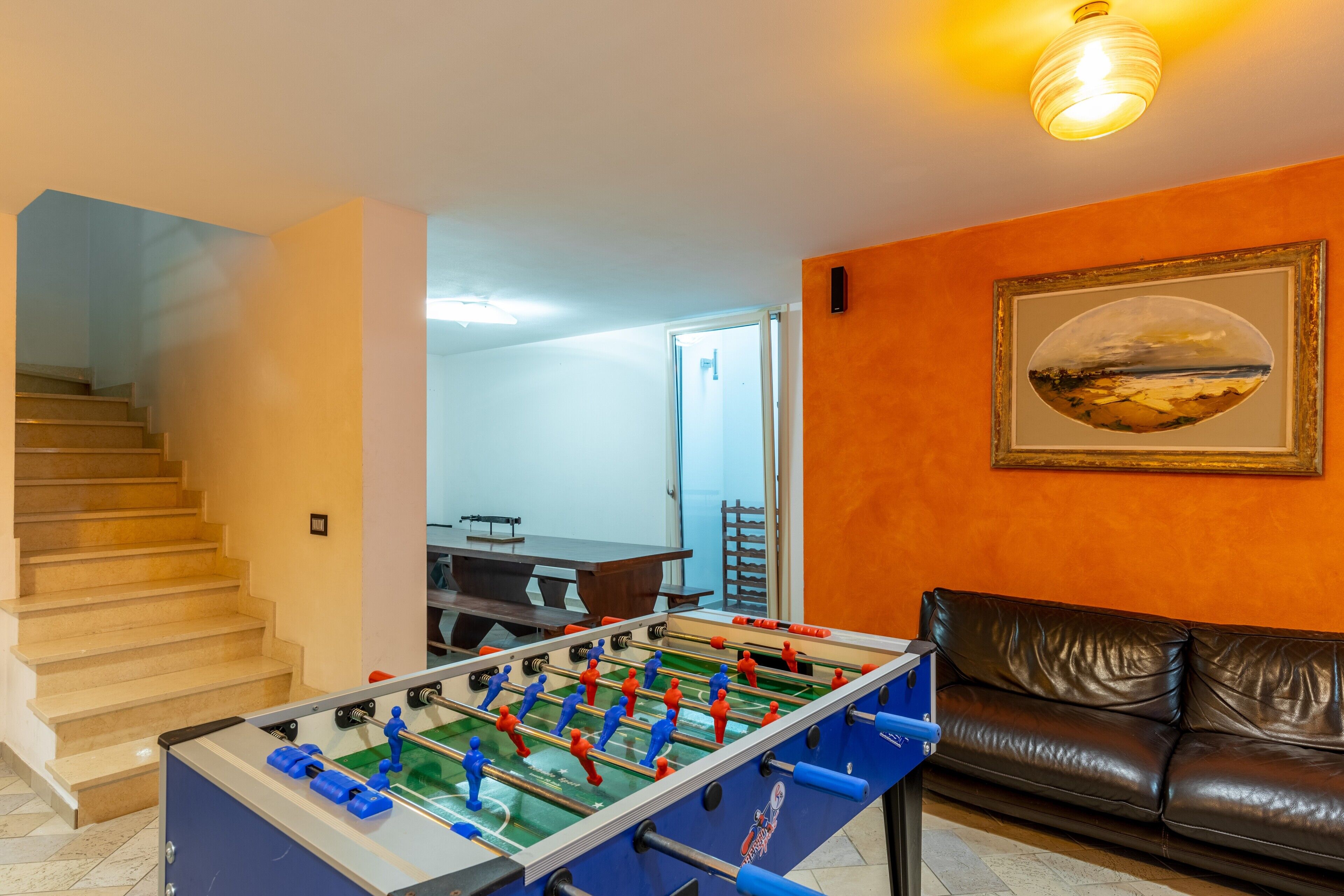 A room with a foosball table, a brown leather sofa, and a staircase.