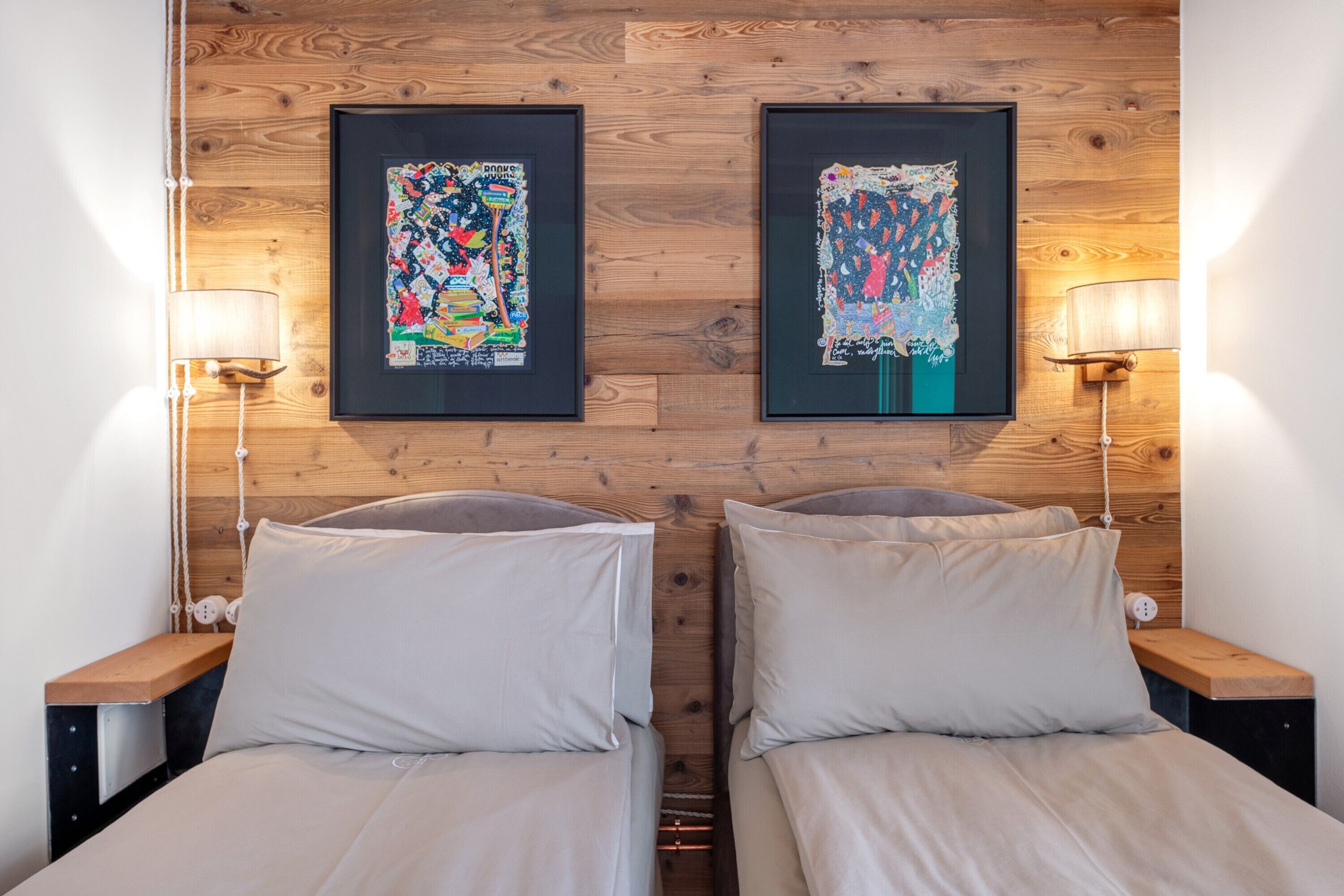 Une chambre double avec deux lits, une tête de lit en bois, des œuvres d’art encadrées, des lampes de chevet et un mur en bois.