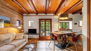 A cozy room with a wooden ceiling, a sofa, a dining table with colorful chairs, and a television. - Chalet 'Nini's Home' with Terrace and Garden with BBQ (Schignano)