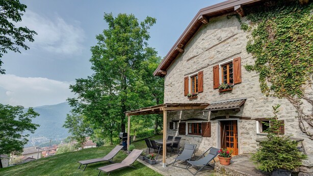 A stone house with a patio, outdoor seating, and a view of the mountains. - Chalet 'Nini's Home' with Terrace and Garden with BBQ (Schignano)