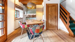 A wooden dining table with colorful chairs, a kitchen in the background, and a staircase. - Chalet 'Nini's Home' with Terrace and Garden with BBQ (Schignano)