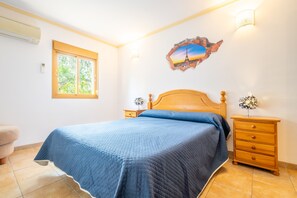 Ein Schlafzimmer mit einem Bett, einem Nachttisch, einer Kommode, einem Fenster und einer Wanddekoration.