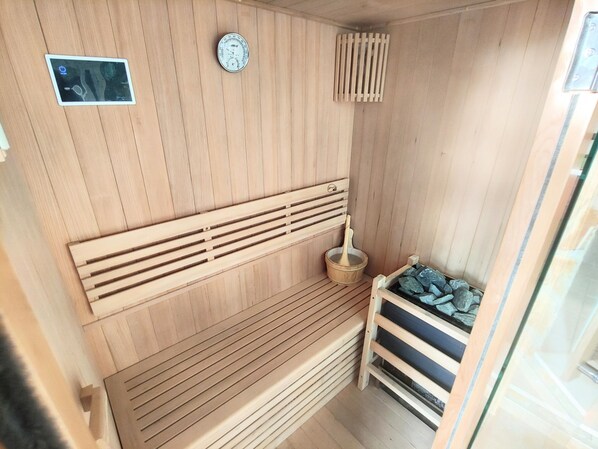 A wooden sauna with a bench, a thermometer, and a bucket with a wooden mallet.