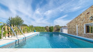 En swimmingpool med en stenvæg, et træhegn og en klar blå himmel.