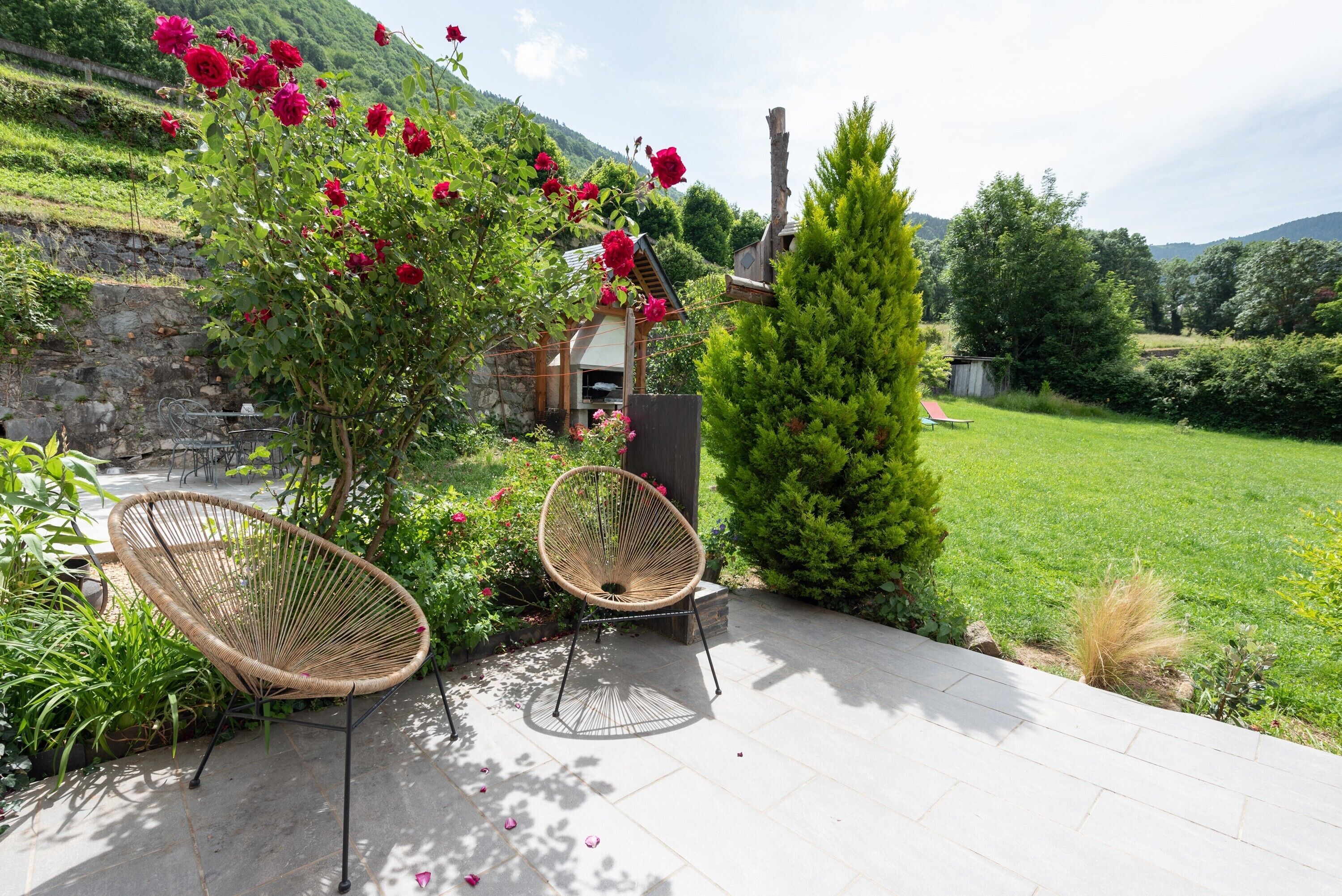 Un patio con dos sillones de mimbre, un muro de piedra y vistas a un paisaje verde.