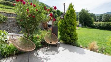 Un patio con dos sillones de mimbre, un muro de piedra y vistas a un paisaje verde.
