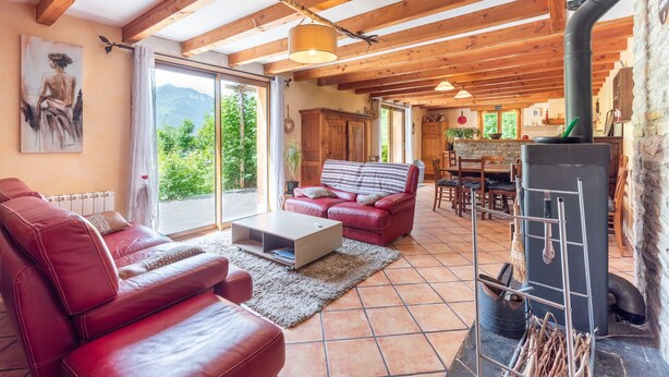 A cozy living room with a red leather sofa, a wooden dining table, and a fireplace.
