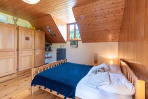 A bedroom with a wooden ceiling, a bed with a blue blanket, wooden cabinets, and a window.