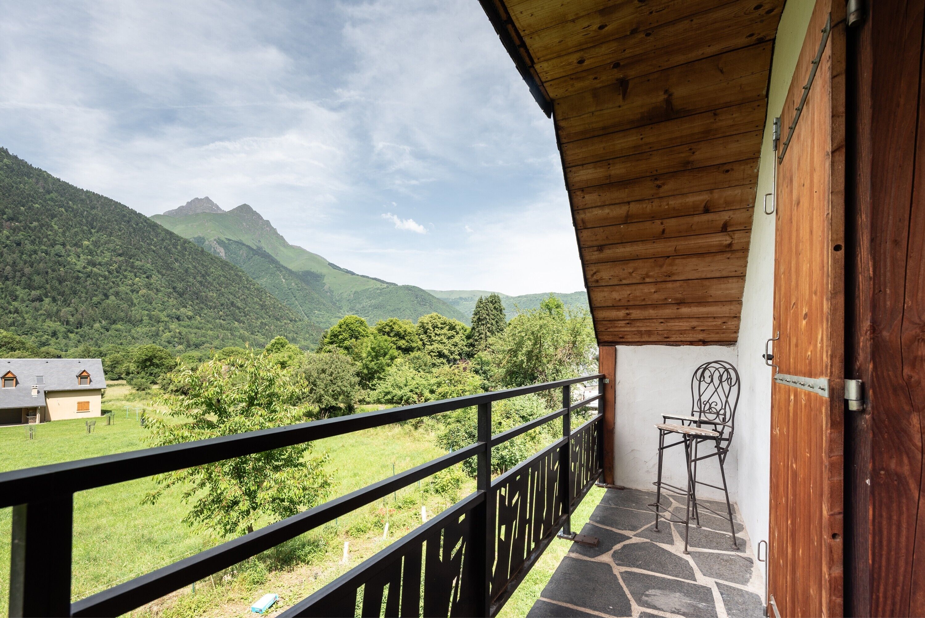 Un balcón con vistas a un paisaje montañoso, una silla y una puerta de madera.