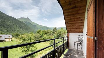 Un balcón con vistas a un paisaje montañoso, una silla y una puerta de madera.