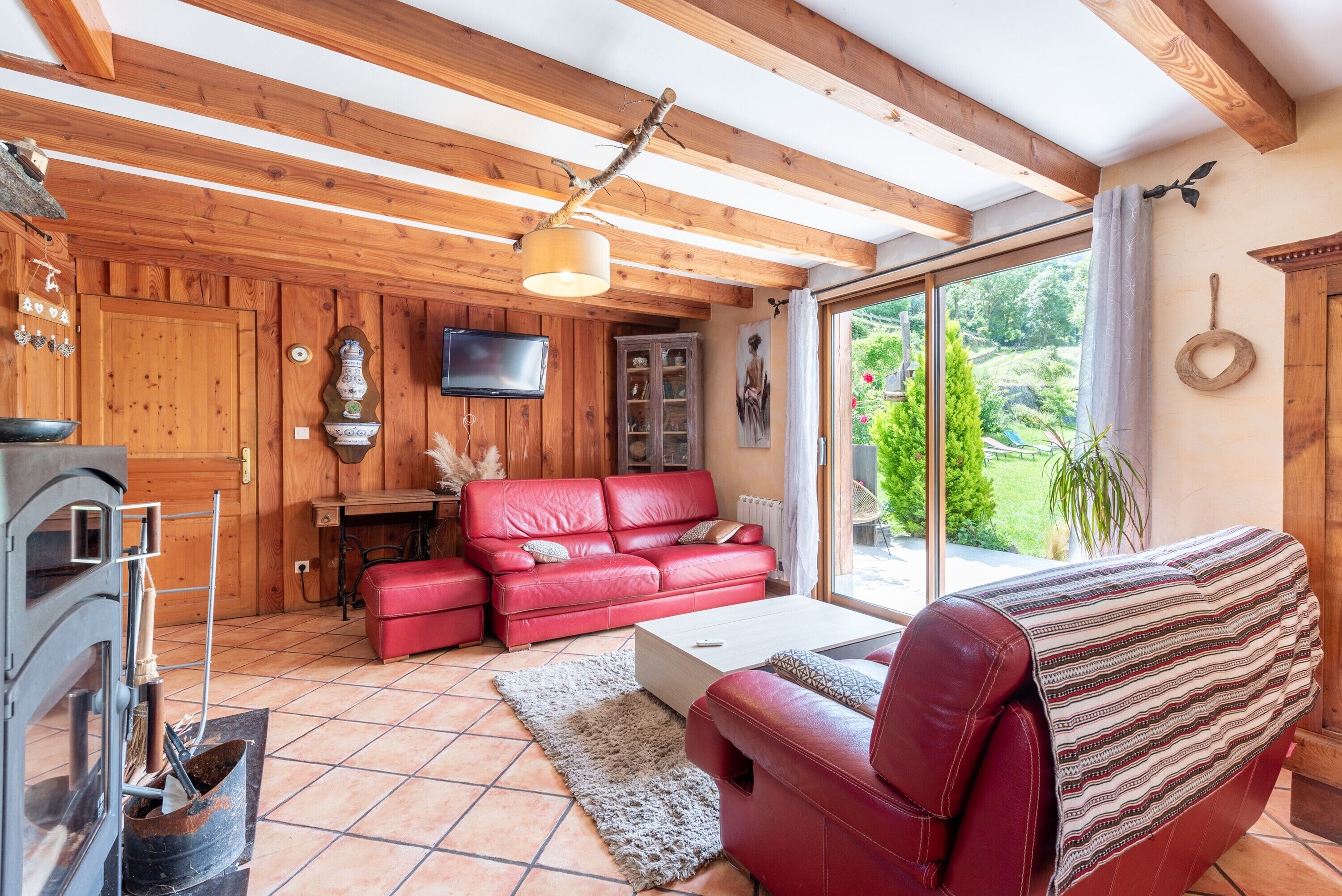 Un interior de madera con un sofá de cuero rojo, una chimenea y un ventanal con vistas a la vegetación.