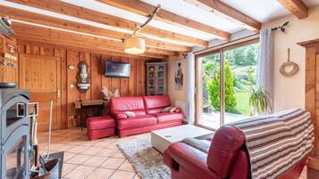 Un interior de madera con un sofá de cuero rojo, una chimenea y un ventanal con vistas a la vegetación.