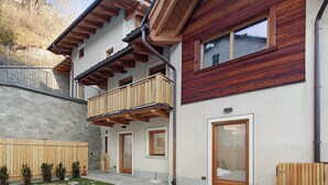 Un edificio moderno con balcón de madera, pared de piedra y cerca de madera.